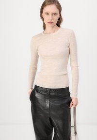 Lys beige ribbet langermet topp med rund hals, kombinert med høyt liv svarte glansfulle skinnbukser og en lys veske.