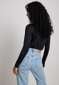 Maglietta nera a maniche lunghe abbinata a jeans chiari a vita alta con etichetta beige sulla parte posteriore del cinturino e tasche curve.