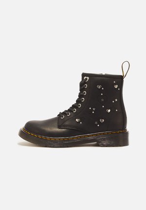 Zwarte leren veterlaars met gele stiksels, versierd met kleine zilveren hart- en sterrenstuds aan de zijkant.