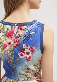 Hihaton kukkamekko, jossa on sininen liukuväri, koristeelliset niitit kauluksessa ja sekalainen vaaleanpunaisen ja vihreän kukkakuosin yhdistelmä.