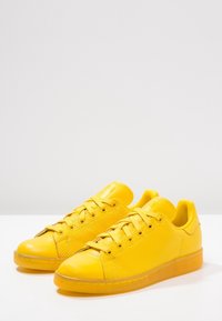 Gula sneakers i syntetmaterial med en slät tåparti, perforerade sidor, platta snören och genomskinliga gummisulor.