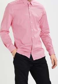 Camicia a maniche lunghe con colletto in tessuto leggero, a motivo checked rosso e bianco. Abbinata a pantaloni neri.