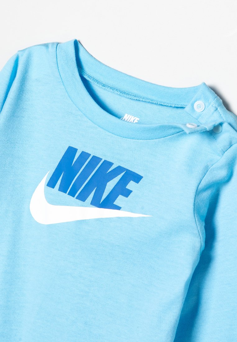 Jasnoniebieski bodysuit dla niemowląt z niebieskim napisem Nike i białym logo swoosh, z guzikami na jednym ramieniu.