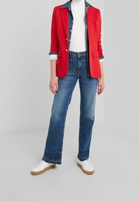 Röd kavaj med guldknappar, vit polotröja, denimskjorta och blå högmidjade jeans. Vita sneakers med bruna sulor.