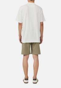 Witte geribbelde t-shirt met korte mouwen, gecombineerd met olijfgroene shorts en wit met zwarte accenten sneakers. Casual pasvorm, textiel met structuur.