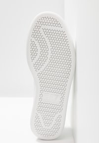 Vit skosula med ett strukturerat hexagonalt mönster och "EA7 Emporio Armani"-logotypen präglad i mitten.