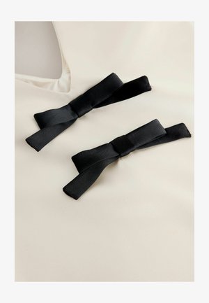 Tessuto crema con due fiocchi di satin neri attaccati. I fiocchi presentano una texture liscia e sono posizionati in modo simmetrico sulla superficie del tessuto.