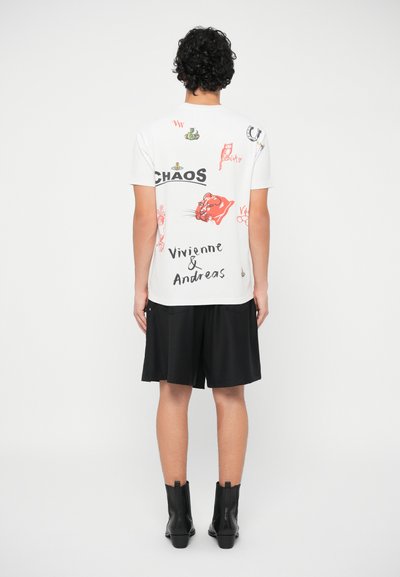 Pessoa vestindo uma t-shirt branca com estampas gráficas coloridas e texto, calções pretos e botas pretas até ao tornozelo, de pé de costas.