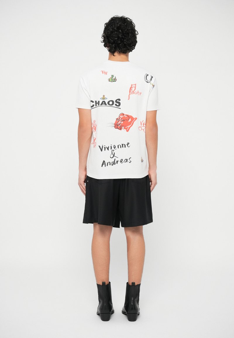 Personne portant un T-shirt blanc avec des imprimés graphiques colorés et du texte, un short noir et des bottines noires, se tenant de dos.