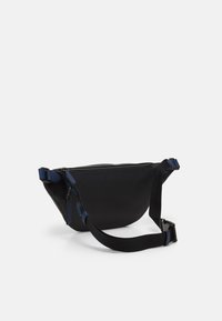 Sac en nylon noir avec un design incurvé, fermeture zippée, bandoulière ajustable et accents bleus. Présente une surface texturée et un style minimaliste.
