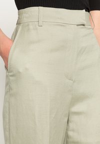 Jasnozielone spodnie wykonane z teksturowanej tkaniny, z bocznymi kieszeniami, gładkim przodem i usztywnionym pasem.