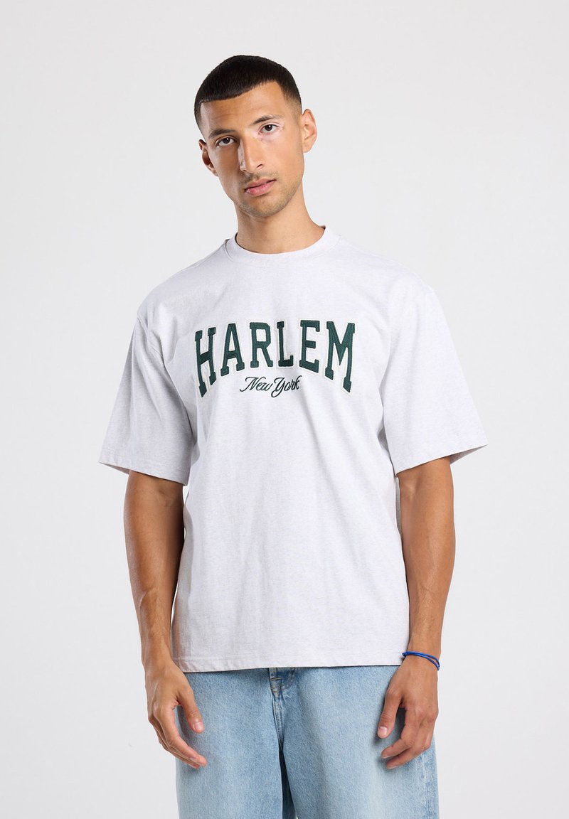 T-shirt gris clair à manches courtes avec le texte en bold vert "HARLEM" et "New York" sur le devant. Coupe boxy avec un col rond.