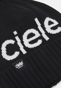 Black knitted beanie featuring a large, white "ciele" logo. Ribbed texture at the base and a small black tag with "ciele ATHLETICS" printed.