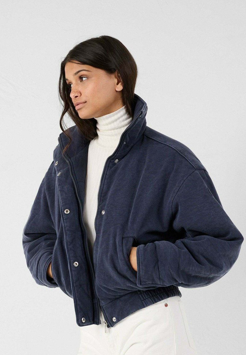 Navyblauwe fleece bomberjack met een hoge kraag, drukknopen en zijzakken. Heeft elastische manchetten en een korter model met een cropped zoom.