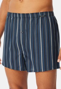 Boxer de rayas azul marino con cintura elástica, que presenta franjas verticales alternas delgadas y gruesas en tonos de azul y gris.