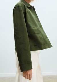 Veste en daim vert avec col chemise, fermeture à boutons sur le devant et deux grandes poches plaquées. Caractérisée par une coupe ajustée légèrement ample.