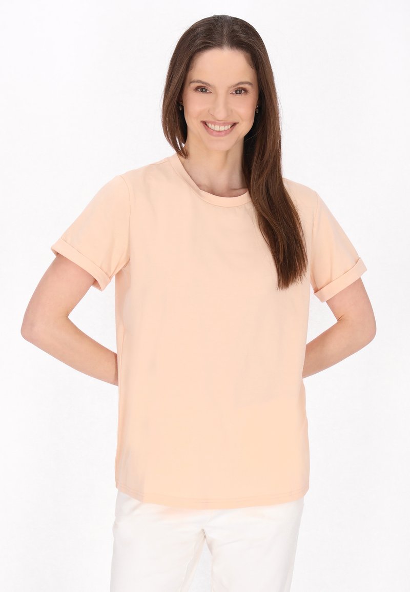 Lys ferskenfarvet kortærmet t-shirt med rund halsudskæring og opsmøgede ærmer, lavet af et glat stof, parret med hvide bukser.