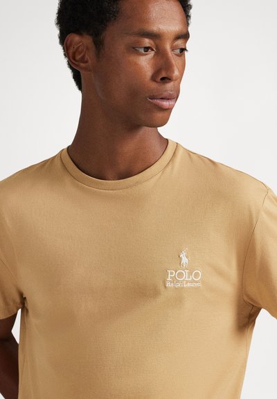 Bēša kokvilnas t-krekls ar apļveida kakla izgriezumu, īsām piedurknēm un baltu izšūtu "Polo Ralph Lauren" logotipu krūšu rajonā.