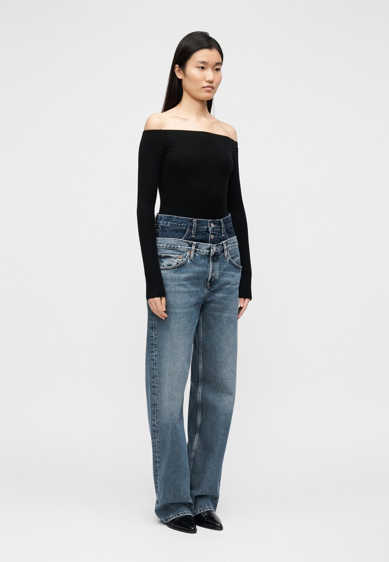Haut noir à épaules dénudées associé à un jean large bleu avec une taille haute, une texture délavée et des détails de couture contrastants.