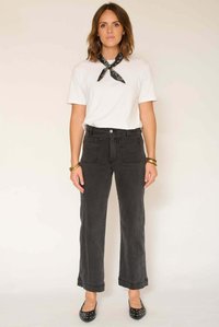 Jean noir à jambes larges avec poches avant, associé à un t-shirt blanc et un bandana noir. Le mannequin porte des ballerines noires et des bracelets.