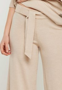 Beige Strick-Hosen mit weitem Bein, einem taillierten Bund und weicher Textur, die eine entspannte Passform und dezente Details betonen.