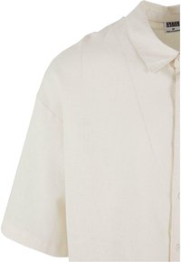 Camicia a maniche corte con colletto in tessuto bianco sporco. Presenta chiusura con bottoni sul davanti e vestibilità ampia con texture sottile.