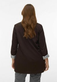 Blazer long marron avec une coupe légèrement oversize, présentant des poignets rayés gris et une texture lisse. Détail visible au dos et design décontracté.