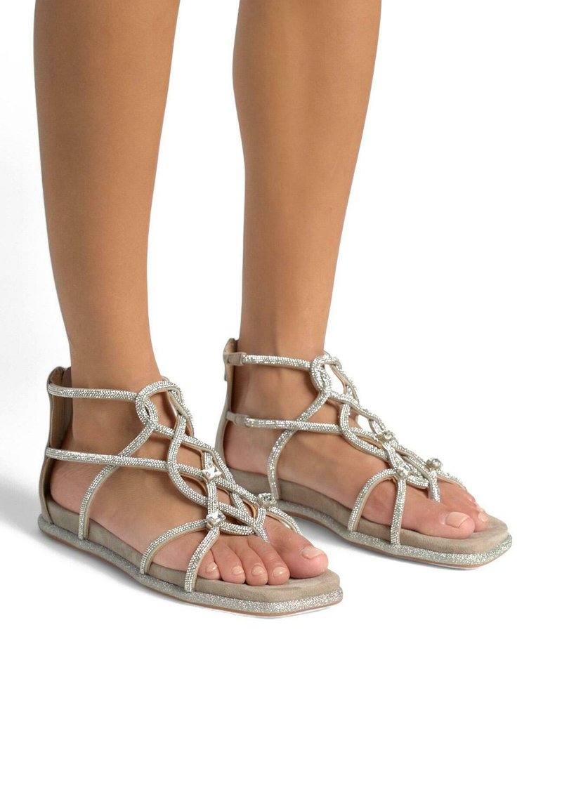 Płaskie sandały z paskami zdobionymi srebrnymi koralikami i miękką, beżową podeszwą, z otwartym noskiem i krzyżującymi się detalami na podbiciu.
