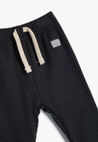 Sorte ribbede bukser med en cremefarvet snøre og et lille "COOL MOOD" logo patch foran. Blødt bomuldsstof.