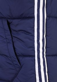 Mörkblå vadderad jacka med vertikala vita ränder, texturerat vadderat material och en sidoficka med triangulär design.