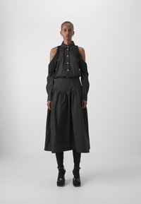 Completo di abbigliamento nero con una maglietta off-shoulder con dettagli di frange e una gonna fluida e arricciata. Tessuto liscio e solido con una vestibilità comoda.