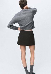 Suéter gris recortado, falda negra y calcetines grises. El suéter tiene una textura suave y un corte relajado. La falda es de línea A y de longitud por encima de la rodilla.
