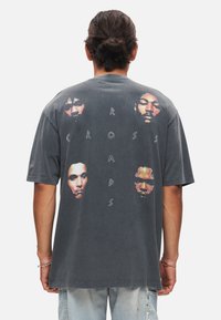 Grå oversized t-shirt med et grafisk print af fem ansigtstræk og teksten "CROSS ROADS" i hvid. Korte ærmer og blød tekstur.