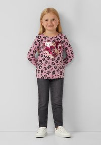Rosa langärmliges Oberteil mit schwarzem Leopardenmuster und einem Pailletten-Herzdesign. Kombiniert mit dunklen Jeans und weißen Sneakers. Glatte Textur.