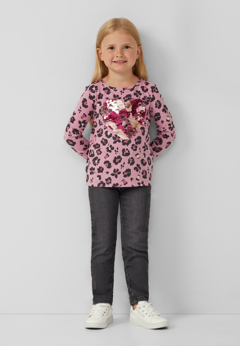 Rosa langärmliges Oberteil mit schwarzem Leopardenmuster und einem Pailletten-Herzdesign. Kombiniert mit dunklen Jeans und weißen Sneakers. Glatte Textur.