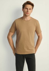 Brązowa koszulka z krótkim rękawem, wykonana z miękkiej bawełny o subtelnej teksturze, z okrągłym dekoltem i małym logo na piersi.