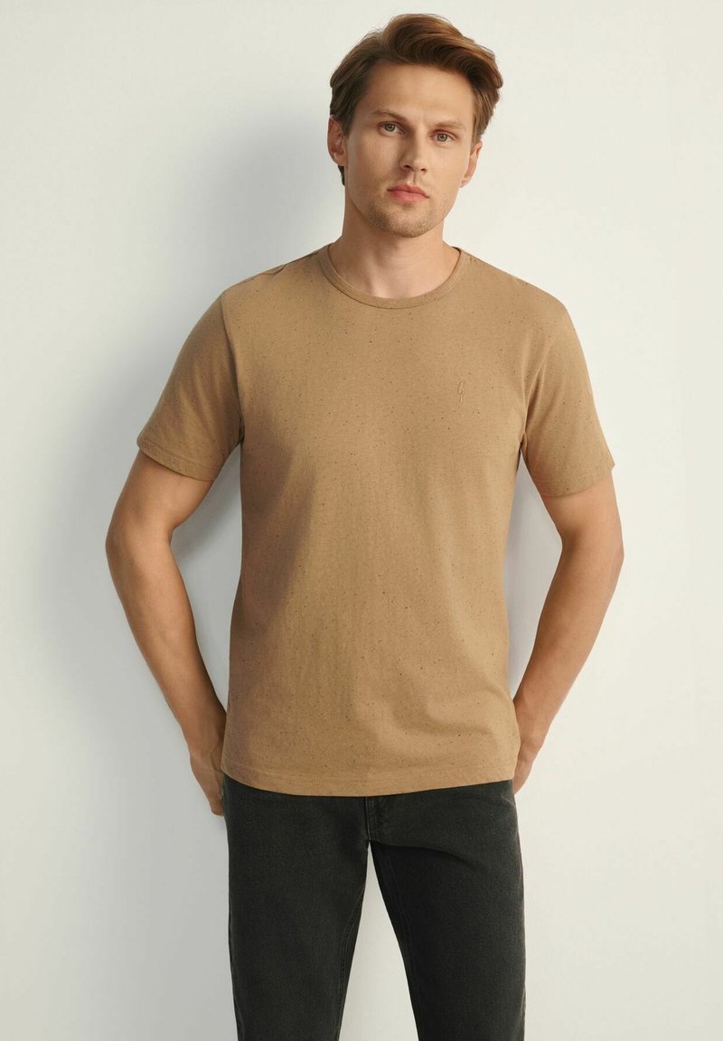 Brązowa koszulka z krótkim rękawem, wykonana z miękkiej bawełny o subtelnej teksturze, z okrągłym dekoltem i małym logo na piersi.