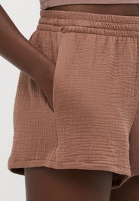 Shorts marron texturés avec une taille élastique et des poches latérales en biais. Le tissu a un aspect froissé et une coupe décontractée.