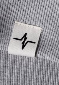 Graues geripptes Material mit einem weißen Etikett, das ein schwarzes Zickzacklinien-Design zeigt, das die Marke oder das Logo anzeigt. Die Textur wirkt weich und dehnbar.