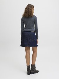 Temno modra jeans krila z dvema zadnjima žepoma, v kombinaciji z oprijetim sivim puloverjem z dolgimi rokavi in črnimi gležnjarji.