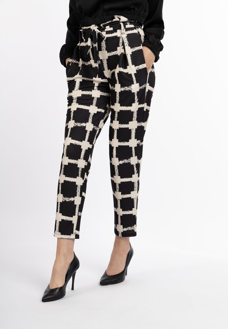 Zwarte en beige gemusterde broek met een ruitpatroon, een taille met riem en zijzakken, gecombineerd met zwarte hoge hakken.