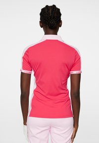 Rosa polo skjorta med vita detaljer, med en klassisk krage och korta ärmar. Tyget är slätt, med en logoband på ärmen.