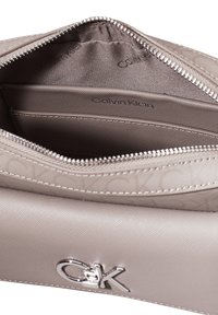 Pánská peněženka Calvin Klein na zip, ve světle taupe texturovaném syntetickém materiálu, má logo jako akcent, hladkou podšívku a vnitřní organizační kapsy.