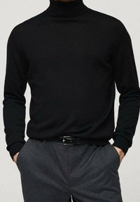 Černý rolákový svetr z měkké pleteniny. Má dlouhé rukávy a přiléhavý střih, kombinovaný se šedými kalhotami na míru a opaskem.