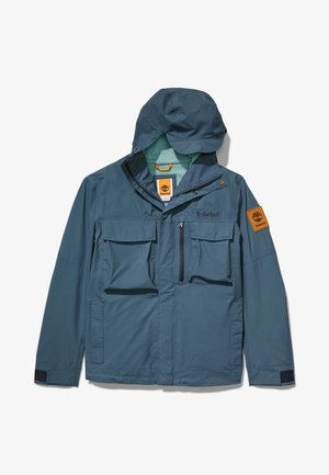 Niebieska kurtka Timberland z kapturem, wieloma przednimi kieszeniami, zapięciem na zamek i guziki oraz naszywką z logo Timberland na lewym rękawie.