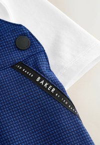 Blaue gemusterte Stoff mit einer strukturierten Oberfläche, versehen mit einem schwarzen Etikett mit weißen Schriftzug und einem runden schwarzen Knopf auf einem weißen Tuch.