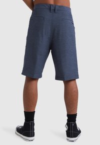 Dunkelblau Shorts aus strukturiertem Stoff, mit zwei Gesäßtaschen und geradem Schnitt. Getragen mit schwarzen High-Top Sneakern und schwarzen Socken.