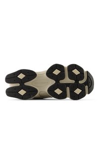 Semelle de chaussure de sport noire et beige avec une surface texturée, présentant des motifs hexagonaux et un logo. Conçue pour la traction et la durabilité.