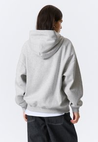 Szara bluza z kapturem o luźnym kroju. Posiada ściągacze przy mankietach i u dołu, oraz materiał dresowy o miękkiej fakturze. Nosi się ją na białej koszuli.