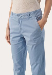 Lichtblauwe katoen broek met een getailleerde pasvorm, zijzakken en een soepele textuur. Plat voorkant met riemlussen en subtiele stikdetails.